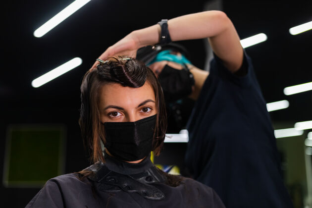 理发师一个专业的女理发师给客户理发这个女孩戴着面具坐在美容院里流行客户时尚