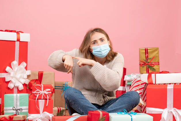 颜色正面图：坐在圣诞节周围的年轻女性戴着无菌面具出现礼物圣诞节围观
