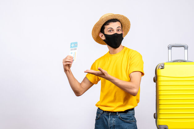 快乐正面图身着黄色t恤的帅哥游客站在黄色手提箱旁举着旅行票手动工具站立手持