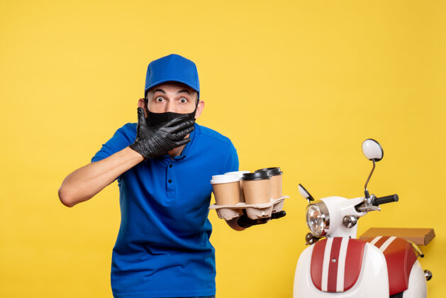 工作正面图：戴着黑色面具的男快递员拿着咖啡在黄色的工作服上递送工作服修理工男性工作