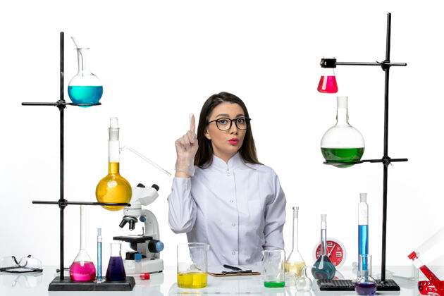 实验室前视图穿着白色医疗服的女化学家坐在白色背景的科学大流行病毒covid实验室里 拿着解决方案葡萄酒药品瓶子