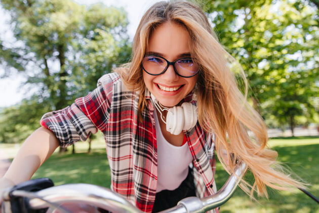 自行车兴奋的女模特戴着眼镜和耳机在公园里兜风情绪激动的金发女孩坐在自行车上大笑娱乐风景成人