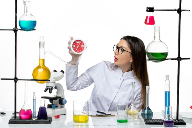 持有前视图穿着白色医疗服的女化学家拿着白色背景上的时钟科学病毒实验室冠状病毒大流行前面计算机视图