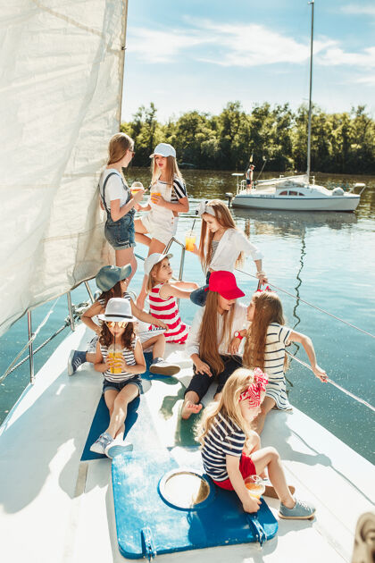 帆船在游艇上喝橙汁的孩子们青少年或儿童女孩对抗蓝天户外女孩朋友航海