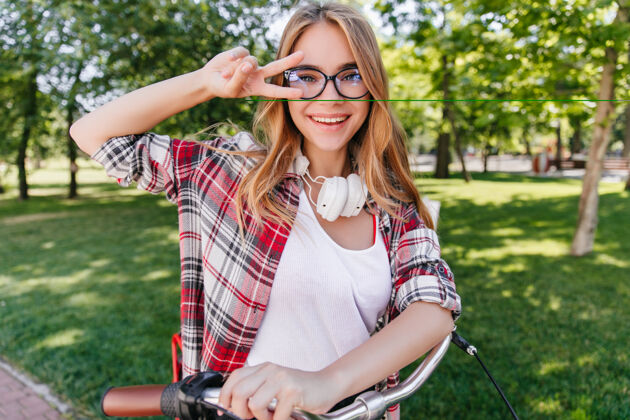快乐可爱的白人女孩骑着自行车的春季照片戴着眼镜和耳机的温文尔雅女模特的户外照片阳光学生乐趣