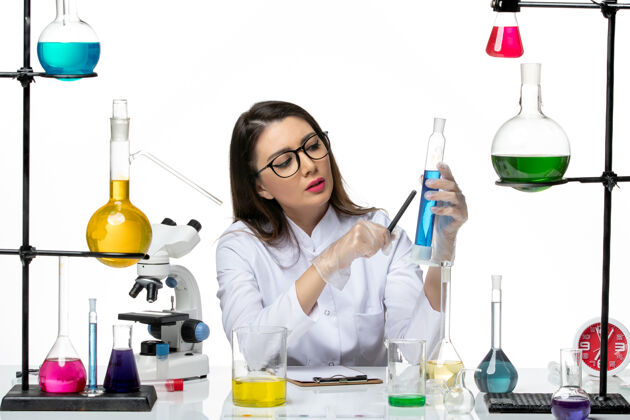 医学前视图穿着白色医疗服的女化学家拿着装有溶液的烧瓶白色背景科学病毒covid-大流行实验室医学实验室烧杯