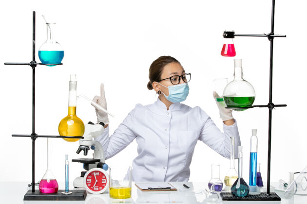 病毒前视图穿着医疗服的女化学家 戴着面罩 白色背景上拿着绿色溶液 飞溅着病毒化学实验室的病毒面罩视图医院