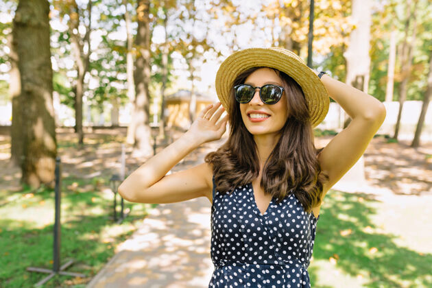 人一个可爱的女人 黑色短发 穿着连衣裙 带着迷人的微笑走在公园里她戴着夏天的帽子和黑色的太阳镜休闲微笑女孩