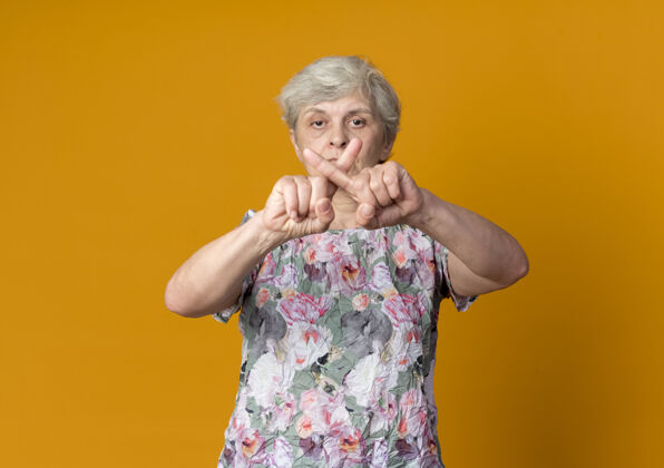 自信自信的老妇人在橙色的墙上交叉手指 表示不孤立老人十字架手指