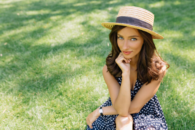白天一个戴着夏天的帽子 穿着夏天的衣服的漂亮女人坐在夏天公园的草地上时尚积极成人