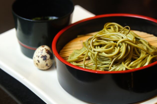 中国菜一碗绿色面条 配鹌鹑蛋和酱汁 放在白色托盘上美味膳食蛋白质