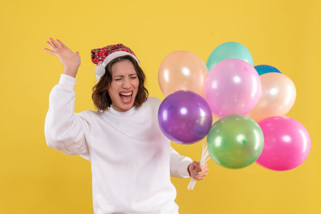 颜色正面图美女手持五颜六色气球在黄色书桌上圣诞彩绘新年女人感慨聚会前面气球