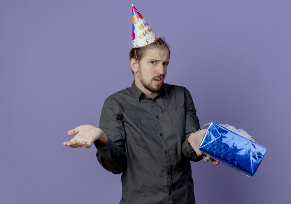迷茫戴着生日帽的迷茫帅哥把礼盒孤立地放在紫色的墙上礼物盒子男人