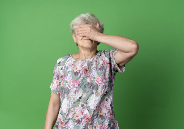 绿不高兴的老妇人闭上眼睛 手被隔离在绿墙上手老闭