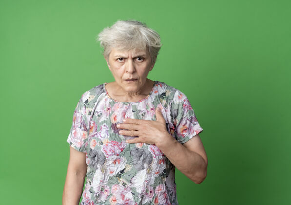 手恼怒的老妇人把手放在下巴上 在绿墙上显得孤立无援女人青老