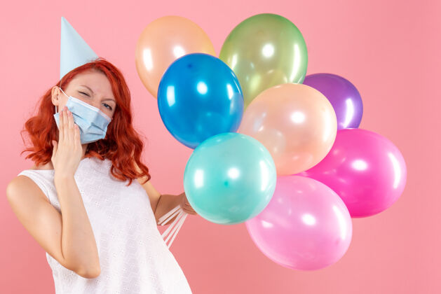 庆祝正面图年轻女性手持彩色气球在粉红色的面具上视图派对病毒