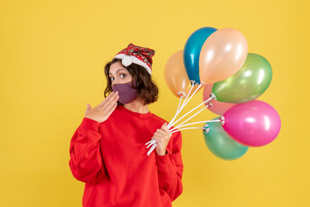 多彩正面图年轻女性拿着气球 戴着黄色的无菌面具前面圣诞节观