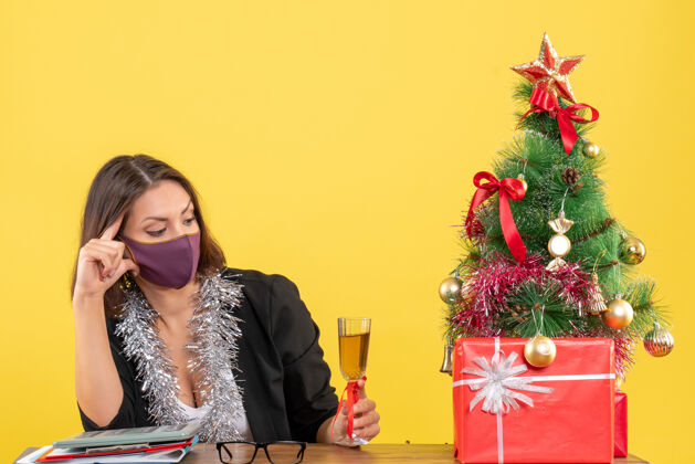 时尚穿着西装戴着医用口罩的美女在黄色的办公室里举杯庆祝圣诞节的心情情绪人医学