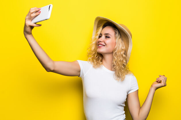 明亮照片中的女孩与手持智能手机的情人进行视频通话 在黄色墙上拍摄自拍享受周末假期手机帽子春天