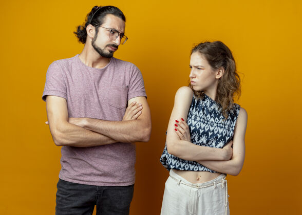 每个人一对年轻夫妇站在橙色的背景上皱着眉头看着对方皱眉年轻人夫妻