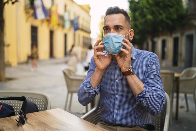 白人身穿蓝色衬衫 戴着医用面罩的年轻男性坐在户外咖啡馆-covid-19概念男性成人医学