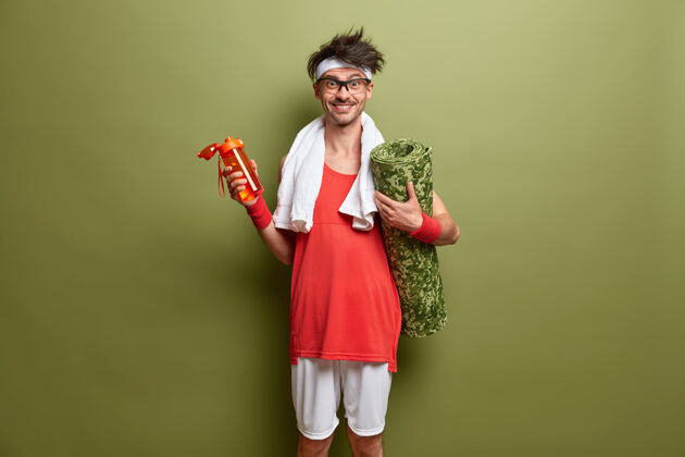 口渴开朗的运动型男人 带着卡雷马特和一瓶水 去锻炼身体 精力充沛 经常锻炼 站在绿色的墙壁上健身健康理念反应眼镜水合