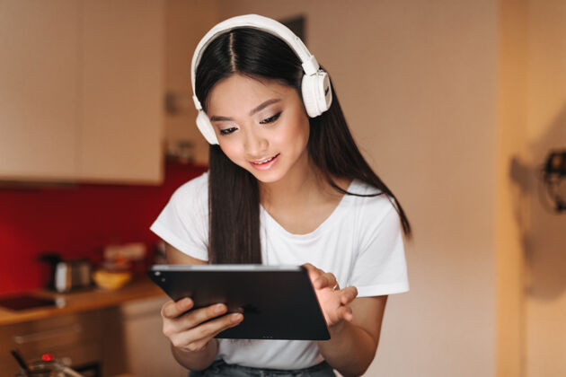 音乐身穿白色上衣 头戴耳机的黑发女人心情大好地看着平板电脑的屏幕空气用户舒适