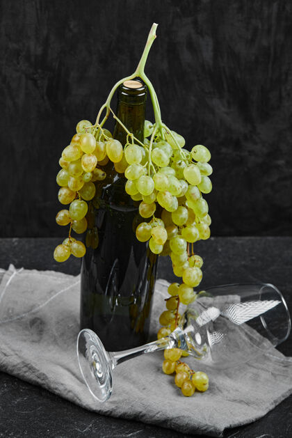 多汁白葡萄围绕着一瓶葡萄酒和一个空杯子 背景是灰色的桌布高质量的照片成熟串自然