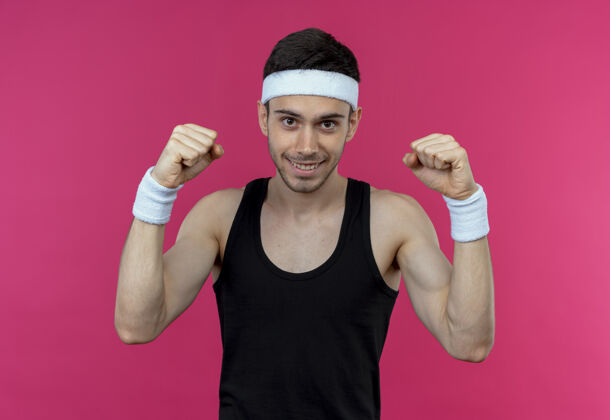 运动戴着头巾的年轻运动型男子举起拳头 站在粉红色的背景上愉快地微笑着站立举起欢呼