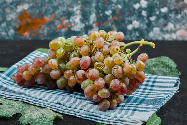 新鲜深色的桌子上放着一束红葡萄和蓝色的桌布高质量的照片季节自然有机