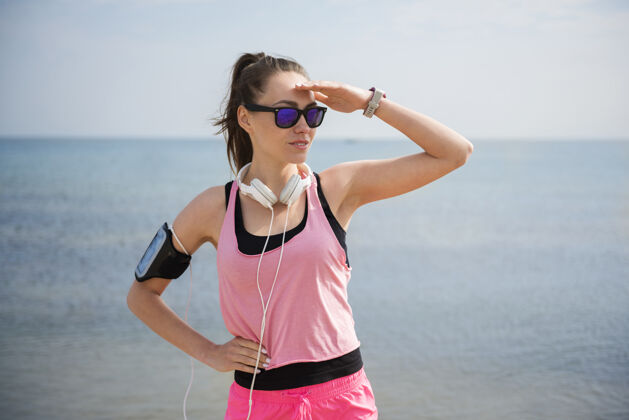 手机特写在海边慢跑的健康年轻人耳机运动训练女