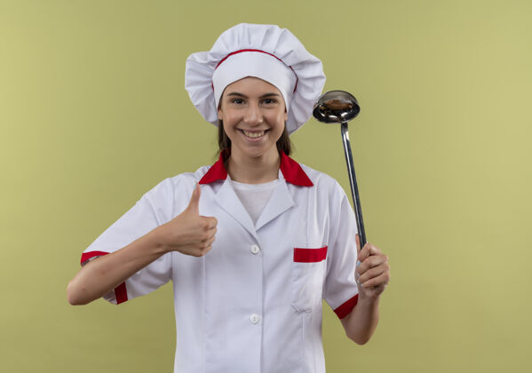 女孩身着厨师制服 面带微笑的白人厨师女孩手持勺子 竖起大拇指 与绿色背景隔离 留有复印空间烹饪勺子厨师