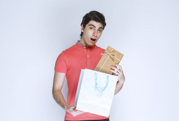 工人一个男人从购物袋里拿出一个纸板礼盒 脸上写着惊喜服装成人姿势