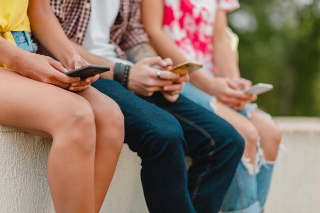 应用快乐的年轻朋友坐在公园里用智能手机微笑公司手机青年情感