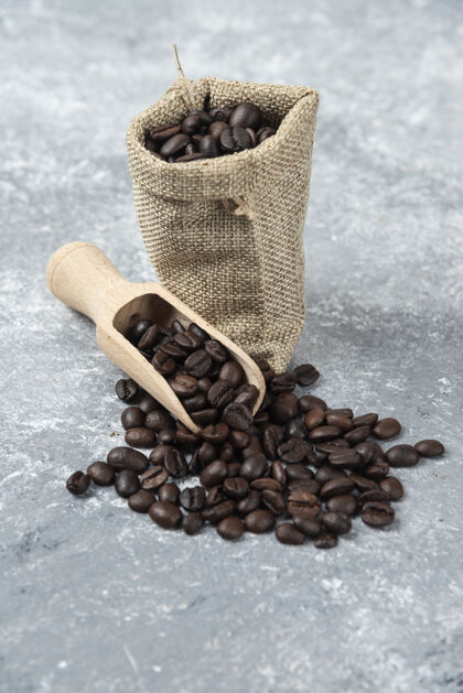 麻布装满烤咖啡豆的麻布和放在大理石表面的木勺浓缩咖啡农作物咖啡