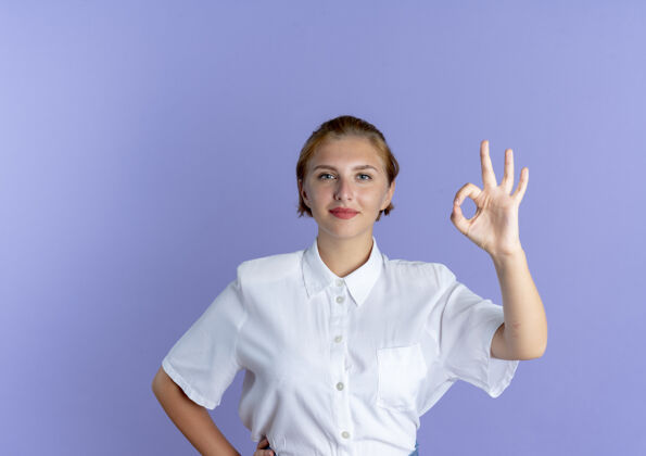 俄国人年轻高兴的金发俄罗斯女孩手势确定手标志孤立的紫色背景与复制空间手好的金发女郎