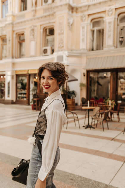 肖像城市里穿着浅衬衫和牛仔裤的快乐女人留着短发和亮嘴唇的现代女人在街上微笑可爱城市欧洲
