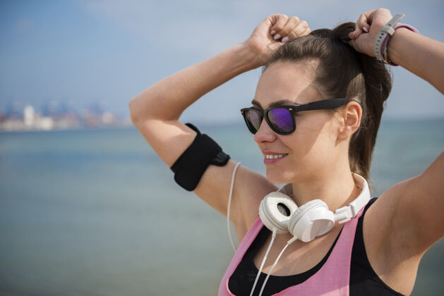 微笑特写在海边慢跑的健康年轻人女人耳机运动训练