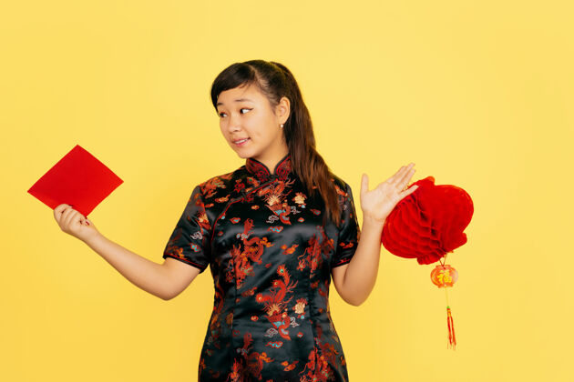 亚洲带着灯笼和信封微笑2020年中国新年快乐黄色背景上的亚洲少女肖像穿着传统服装的女模特看起来很快乐庆祝 情感复制空间服装新年欢呼