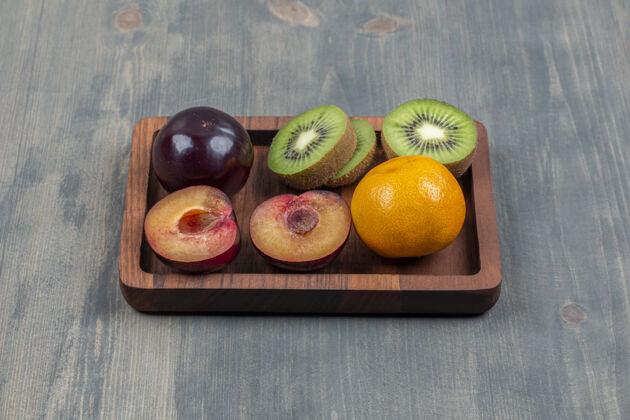 李子把新鲜的猕猴桃切成片 放在木板上 配上橘子和李子食物猕猴桃木板