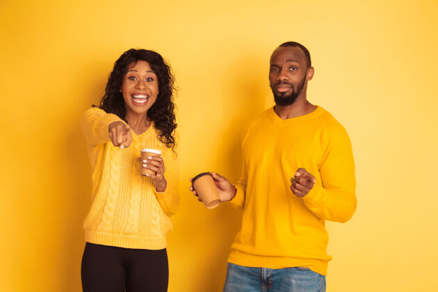 微笑年轻感性的非裔美国人男女 穿着黄色背景的明亮休闲服美丽的情侣人类情感的概念 面部表情 关系 广告喝咖啡和指点女孩休闲金融