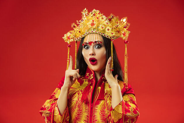 微笑中国传统的优雅女子在摄影棚的红色背景美丽的女孩穿着民族服装中国新年 优雅 优雅 表演者 表演 舞蹈 女演员 服装的概念文化脸女孩