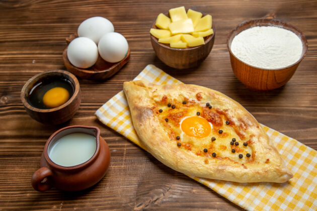 面包正面图美味的鸡蛋面包刚从烤箱里拿出来 在棕色桌子上放上牛奶和奶酪面团 烤面包 包蛋早餐比萨饼牛奶