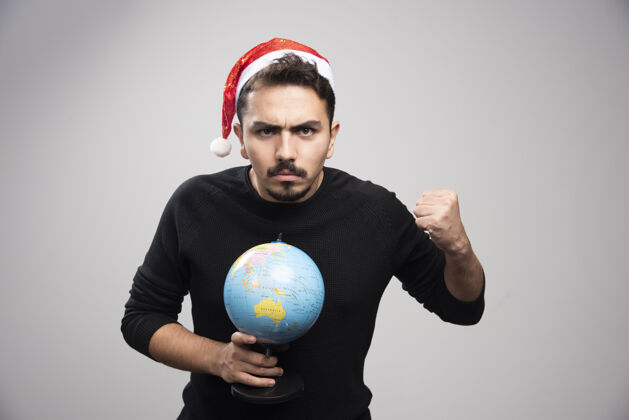 男人一个戴着圣诞老人帽子的愤怒的男人伸出拳头拿着地球仪模型圣诞老人男孩