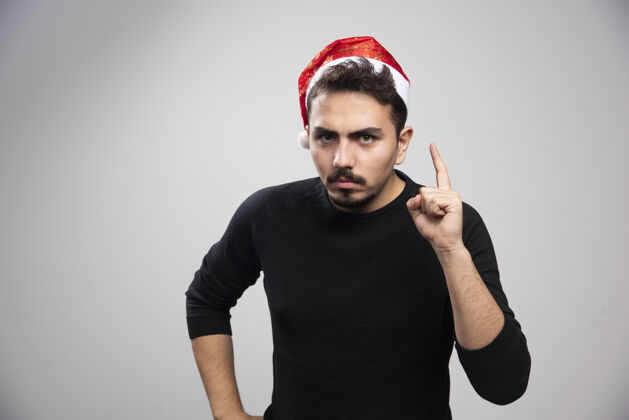 肖像一个严肃的黑发男人戴着圣诞老人的帽子 竖起手指摆姿势人类男人男人