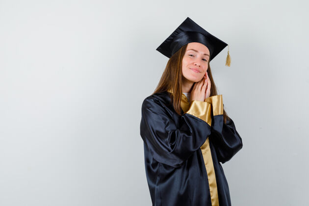 持有年轻的女毕业生手拉着脸颊 穿着学院服 看起来很漂亮正面图时尚前面学术
