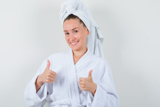 成人穿着白色浴衣 毛巾的年轻女士竖起大拇指 看上去很开心正视图模特新鲜拇指