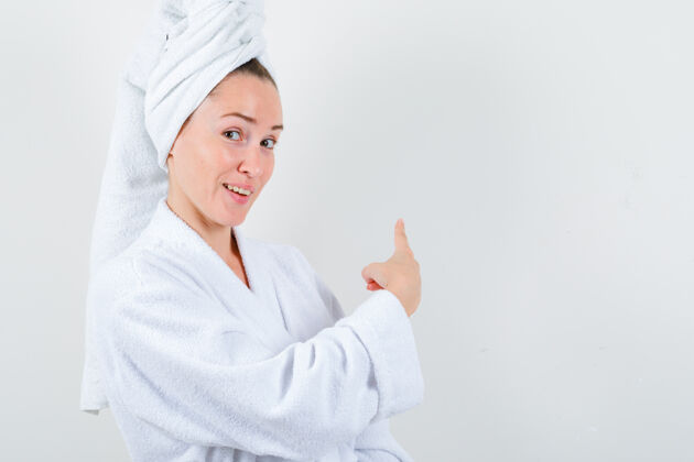 模特年轻的女士指着后面的白色浴衣 毛巾 看起来很快乐前视图完美健康清洁