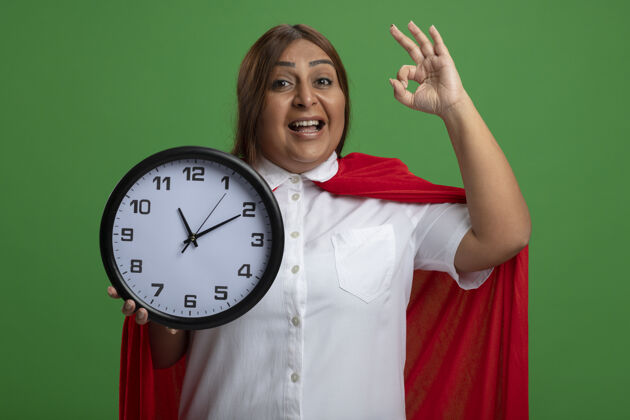 女性微笑的中年超级英雄女性手持挂钟 在绿色背景上显示出良好的姿态中年秀时钟