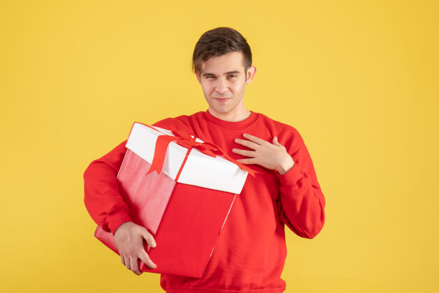 人物正面图：穿着红色毛衣的年轻人拿着黄色背景的圣诞礼物年轻人礼物可爱